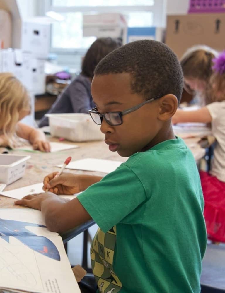 A student focused on writing at a desk in a classroom